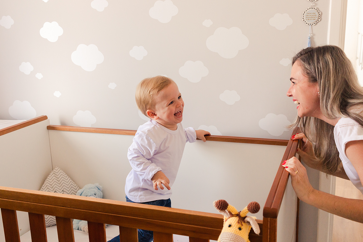 foto de criança dentro do do berço sorrindo para a mãe no ensaio de família em casa na cidade de Sp