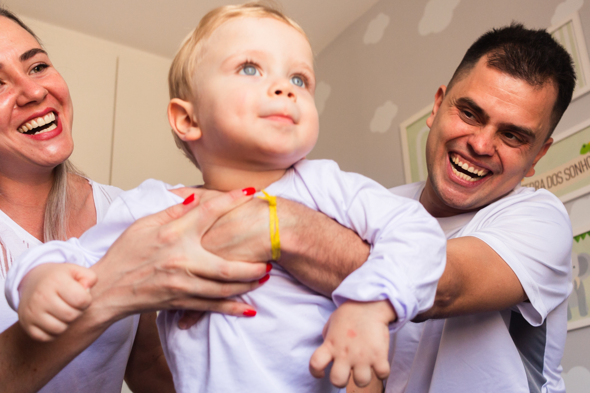foto de criança no colo dos pais sorrindo e brincando dentro do quarto no ensaio de família em casa na cidade de Sp