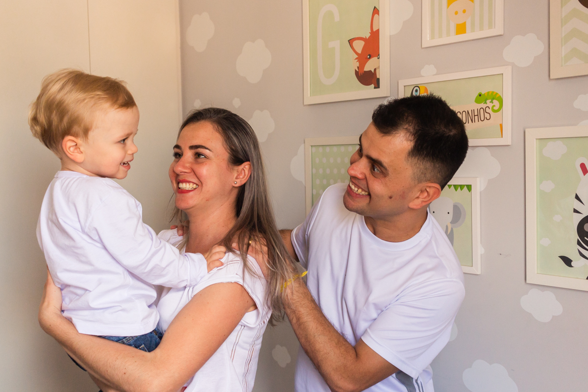 foto de criança no colo dos pais sorrindo e brincando dentro do quarto no ensaio de família em casa na cidade de Sp