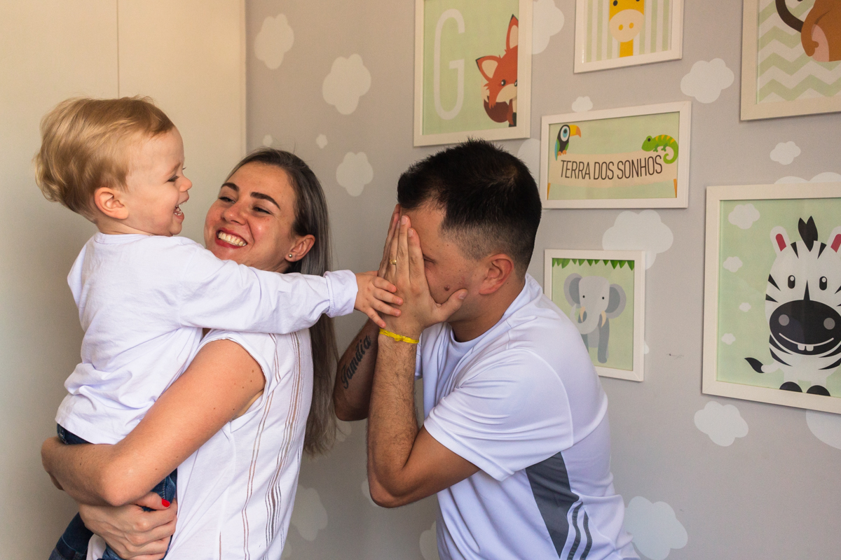 foto de criança no colo dos pais sorrindo e brincando dentro do quarto no ensaio de família em casa na cidade de Sp