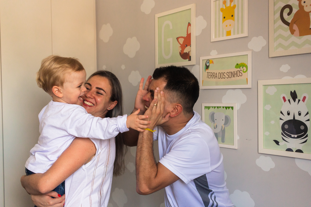 foto de criança no colo dos pais sorrindo e brincando dentro do quarto no ensaio de família em casa na cidade de Sp