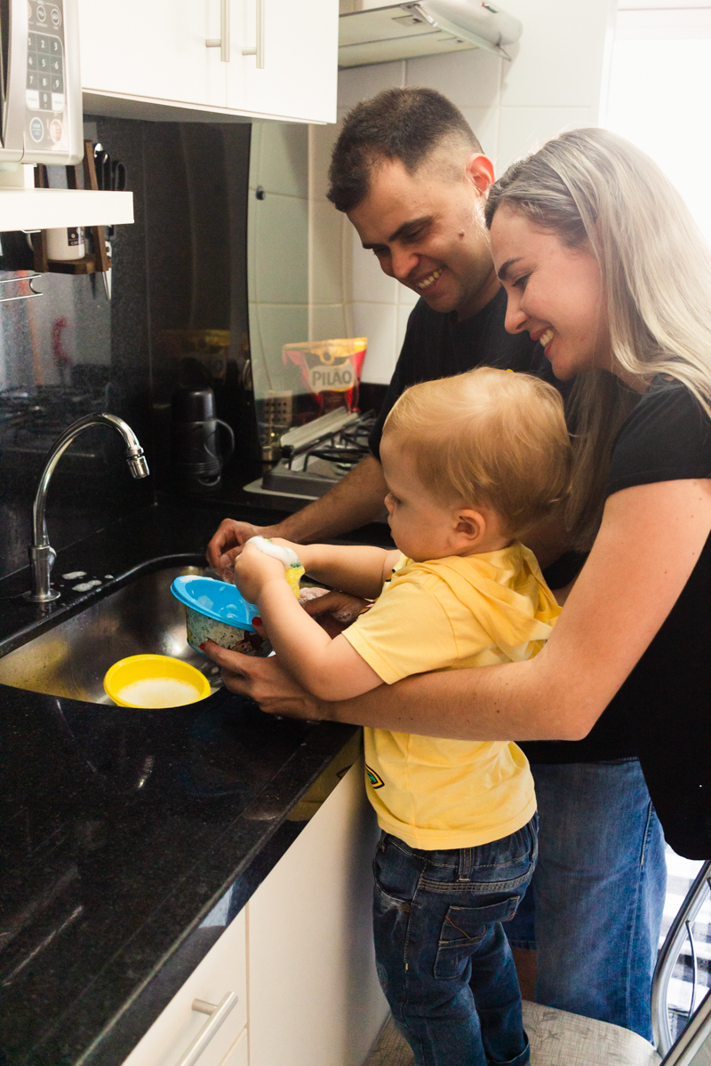 foto de criança lavando a louça com os pais na cozinha no ensaio de família em casa na cidade de Sp