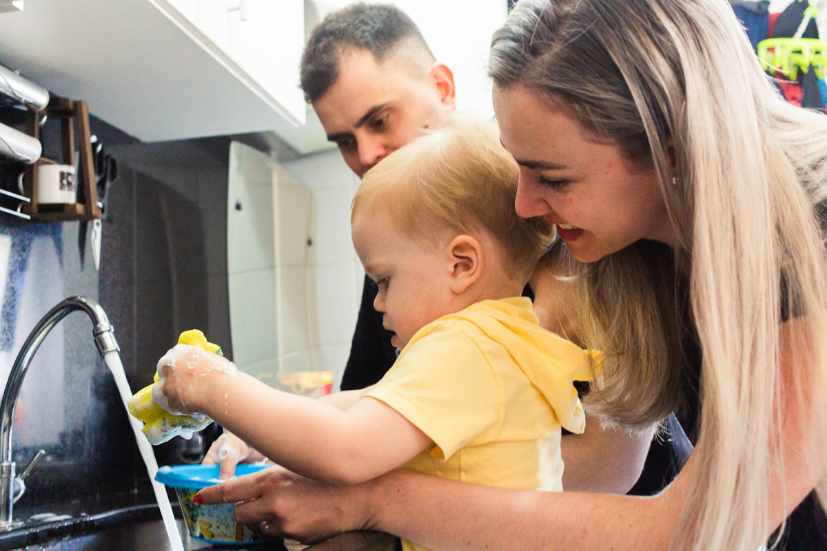 foto de criança lavando a louça com os pais na cozinha no ensaio de família em casa na cidade de Sp