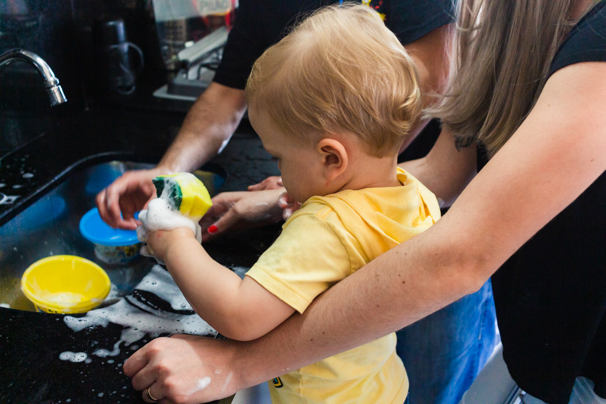 foto de criança lavando a louça com os pais na cozinha no ensaio de família em casa na cidade de Sp