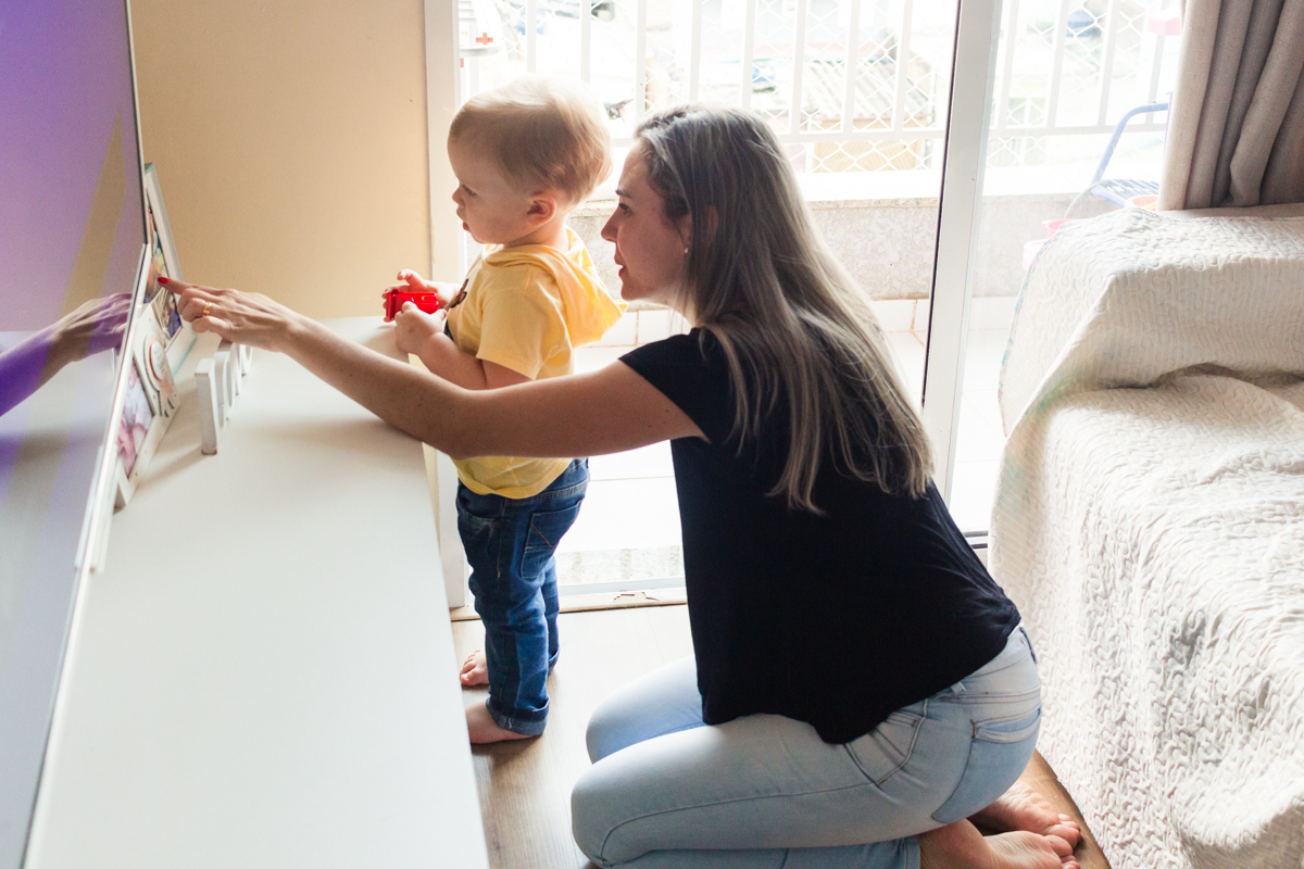 foto de criança olhando porta retratos com a mãe na sala de casa no ensaio de família em casa na cidade de Sp