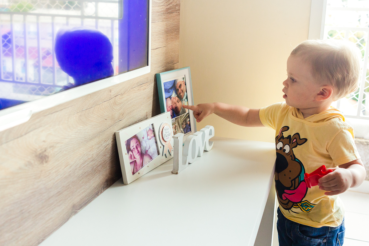 foto de criança olhando porta retratos  na sala de casa no ensaio de família em casa na cidade de Sp