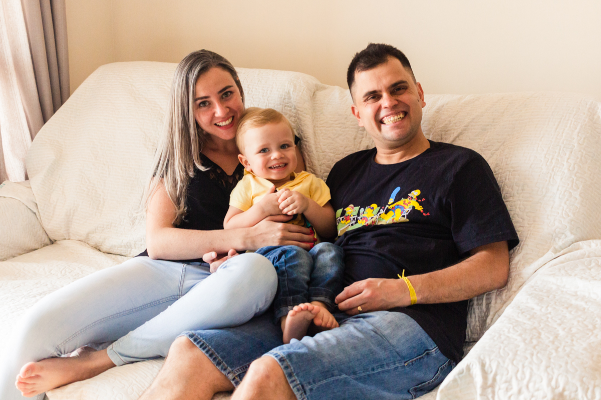 foto de criança sorrindo com os pais sentados n sofá sala no ensaio de família em casa na cidade de Sp