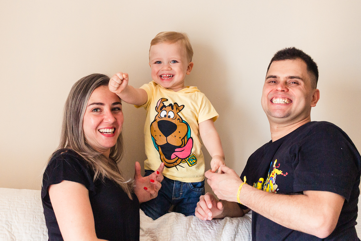 foto de criança sorrindo com os pais sentados n sofá sala no ensaio de família em casa na cidade de Sp