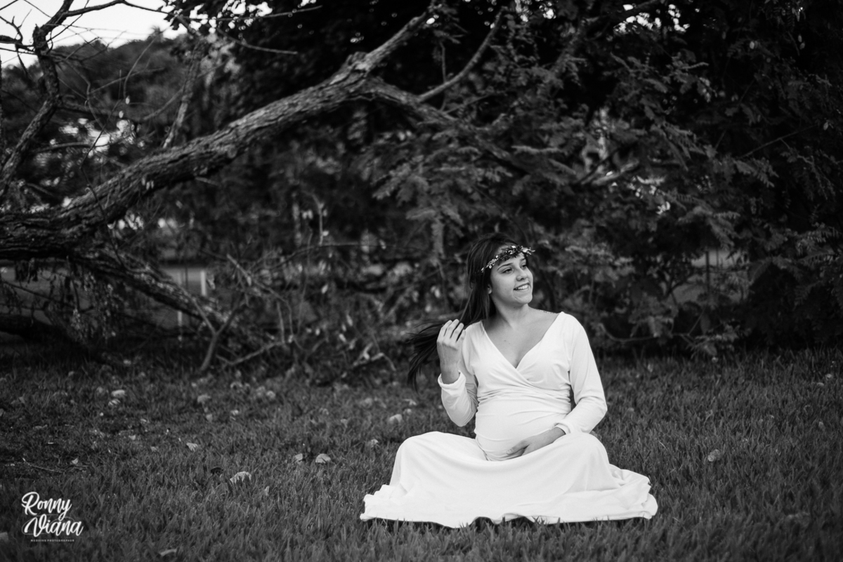 Gestante sentada ao lado da arvore sorrindo arrumando o cabelo no parque da rua do porto em Piracicaba SP fotografia por Ronny Viana