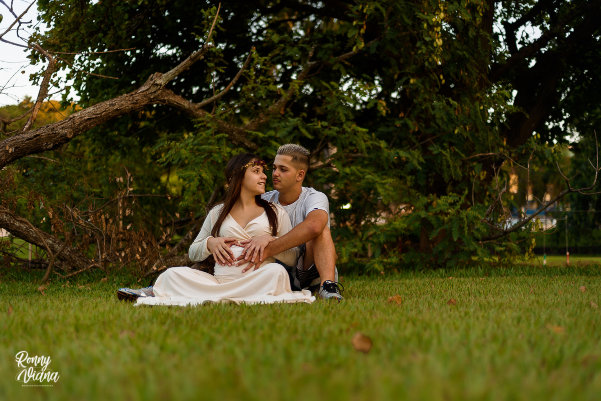 Casal sentados no chão ao lado da arvore caida com as mãos na barriga da gestante em Piracicaba SP foto ronny viana