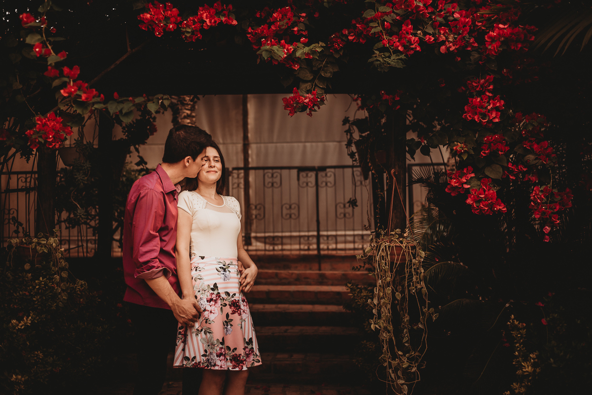 Casal em baixo do ramo de flores vermelhas abraçados beijando em piracicaba por Ronny Viana