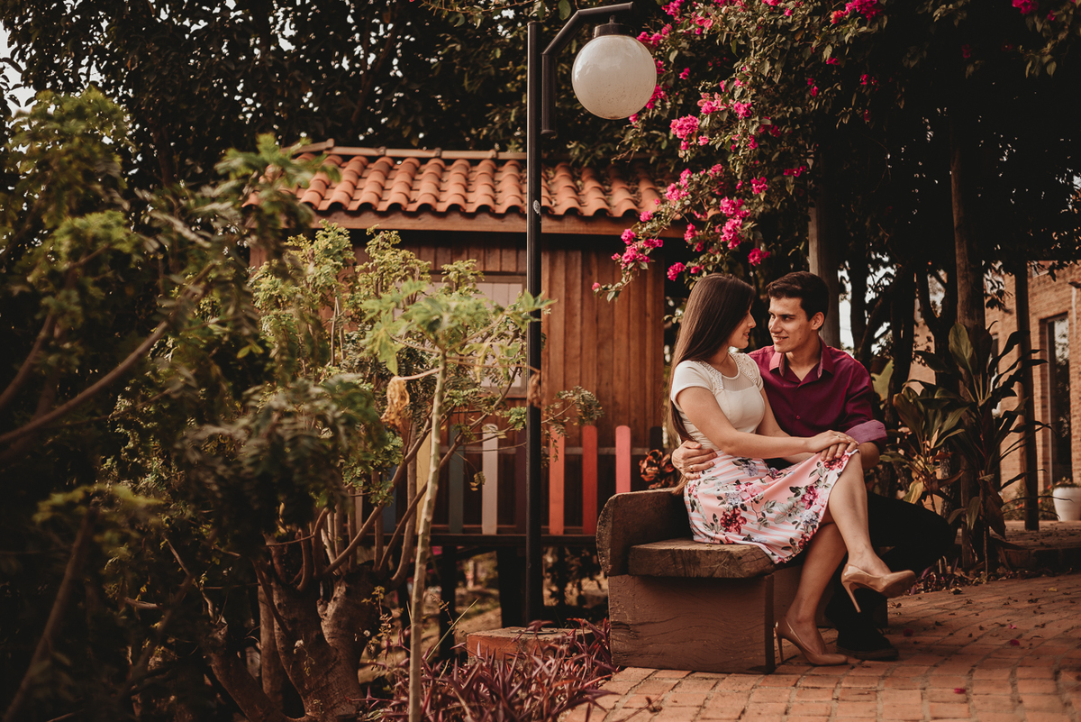 Fotografia do casal em ensaio sentados no banco abraçados trocando carinho