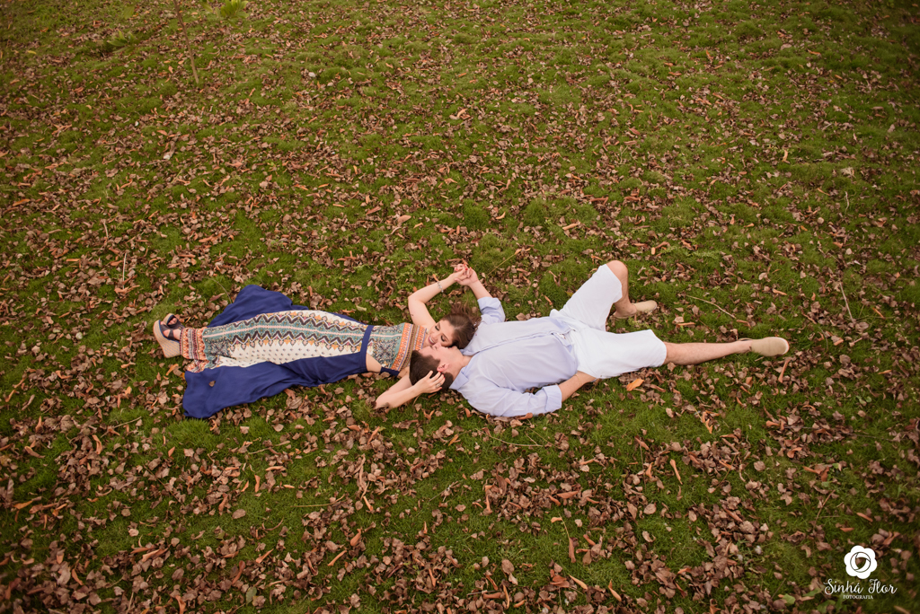 Casal de noivos, Daniele e Thiago, deitados trocando carinho no chão com folhas em Dourados - MS, Sinhá Flor Fotografia