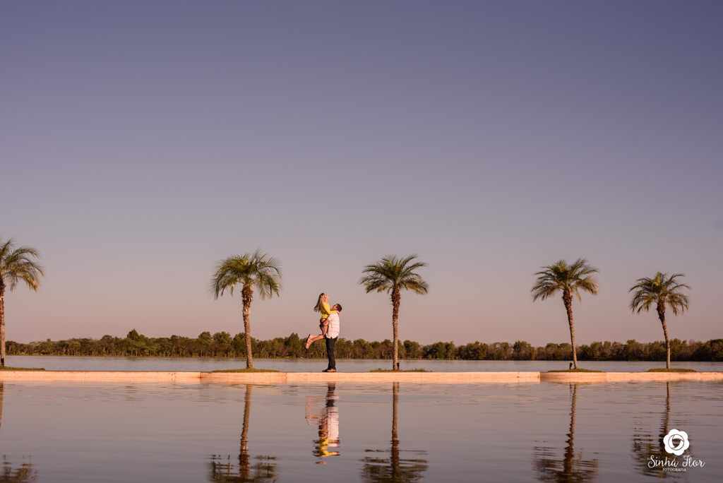 Casal de noivos, Carina e Rodolfo, noivo erguendo noiva com coqueiros ao fundo em Itaporã - MS, Sinhá Flor Fotografia