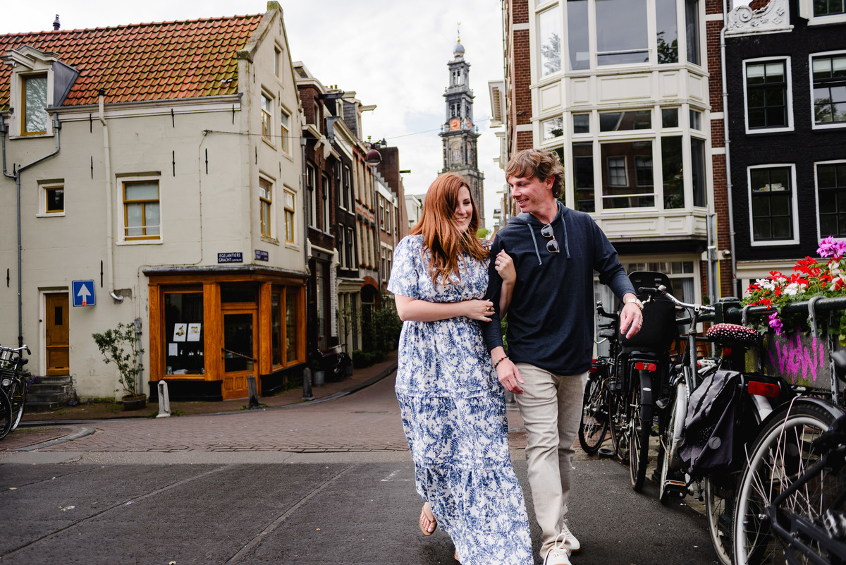 Couple during holiday in Amsterdam during Summer crossing a bridge in the Jordaan with West tower in the background