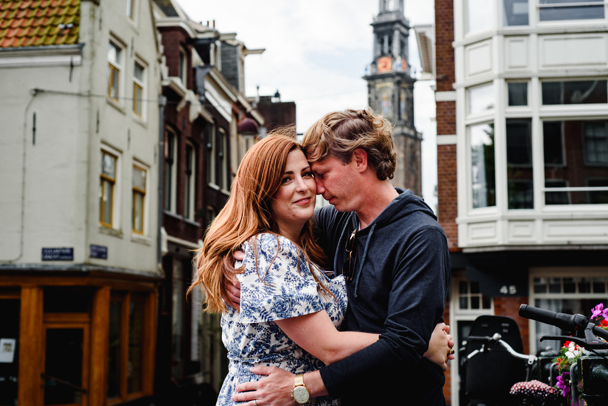 Couple during holiday in Amsterdam during Summer crossing a bridge in the Jordaan with West tower in the background