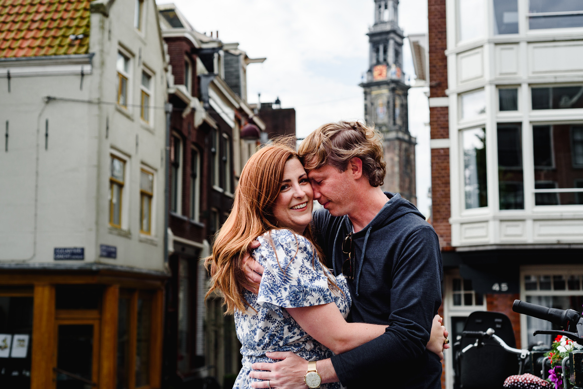 Couple during holiday in Amsterdam during Summer crossing a bridge in the Jordaan with West tower in the background
