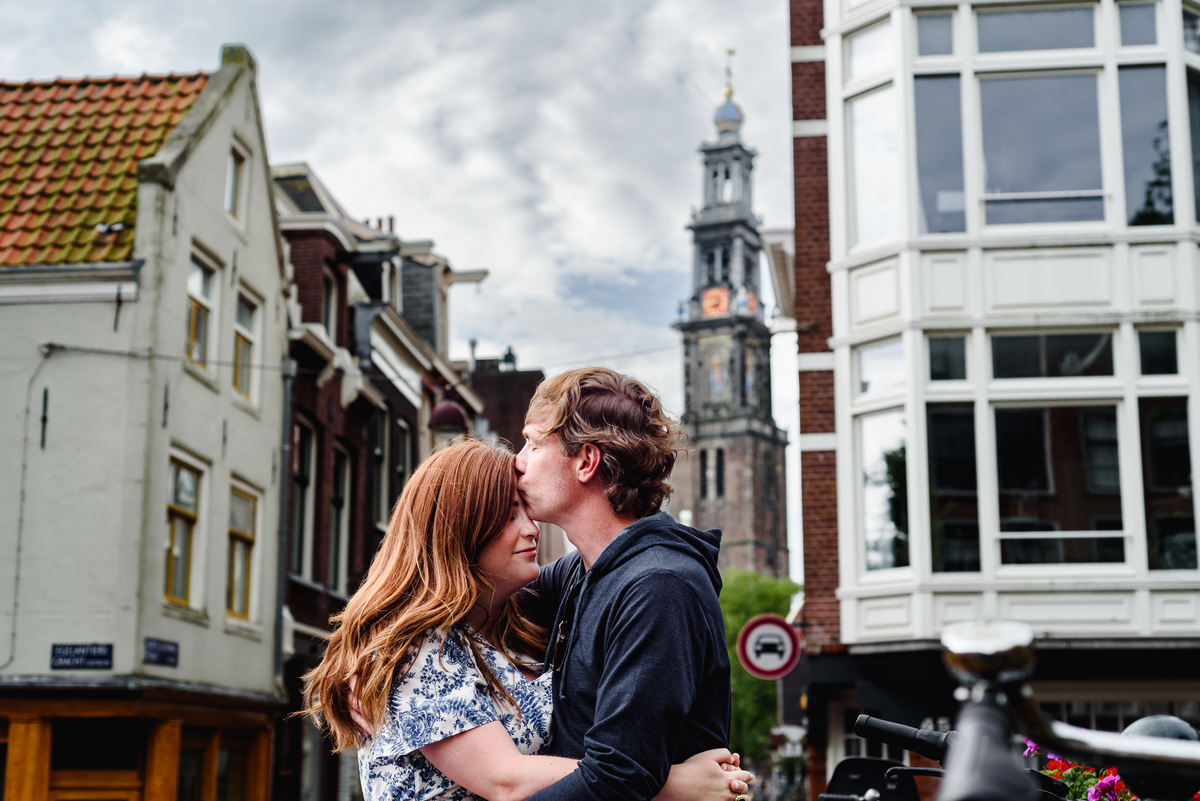 Couple during holiday in Amsterdam during Summer crossing a bridge in the Jordaan with West tower in the background
