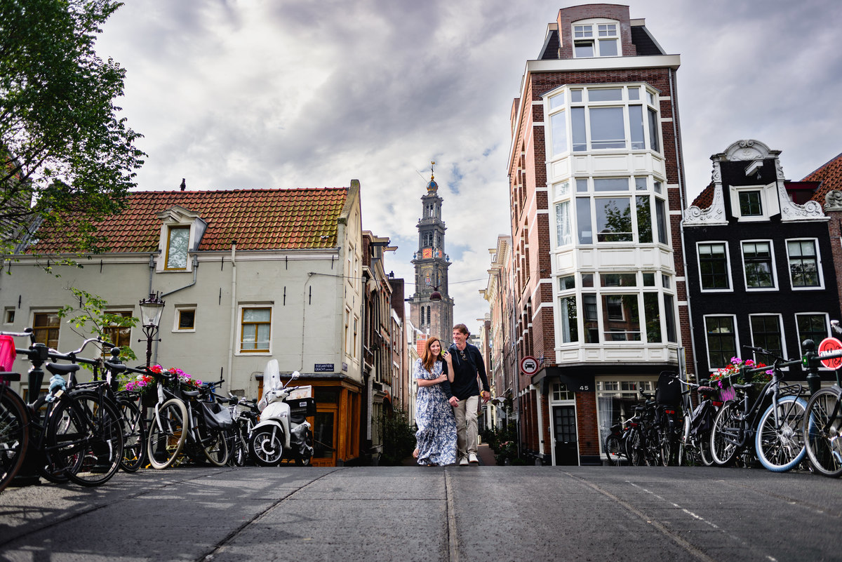 Couple during holiday in Amsterdam during Summer crossing a bridge in the Jordaan with West tower in the background