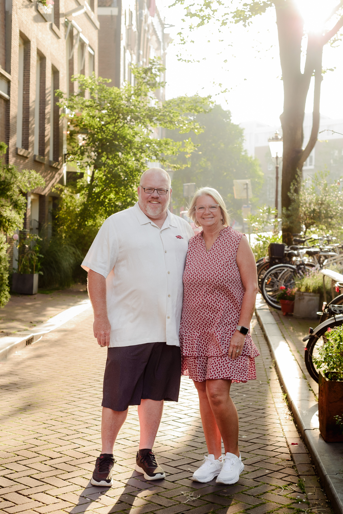 The couple standing close, smiling in the warm sunlight with the greenery and bikes framing the shot.