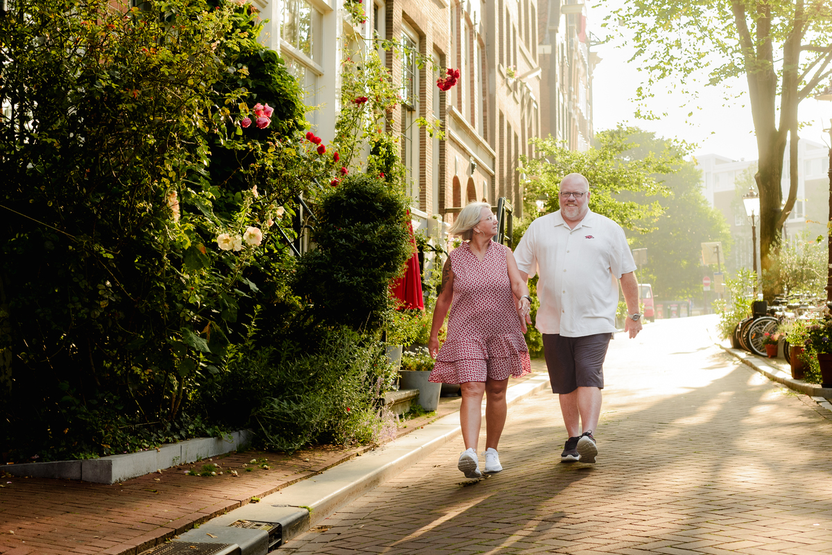 The couple walking down a charming Amsterdam street, surrounded by lush greenery and historic buildings.
