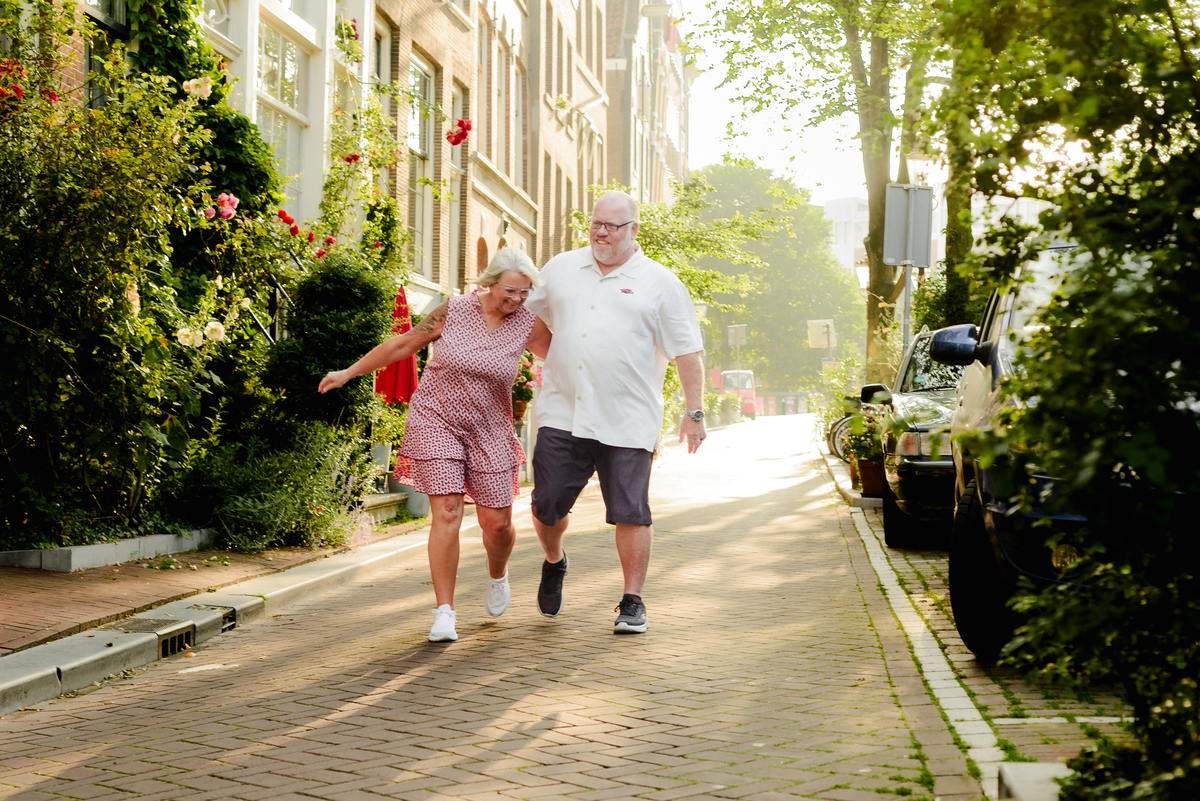 The couple running playfully down a peaceful, tree-lined street in Amsterdam, enjoying their time together.
