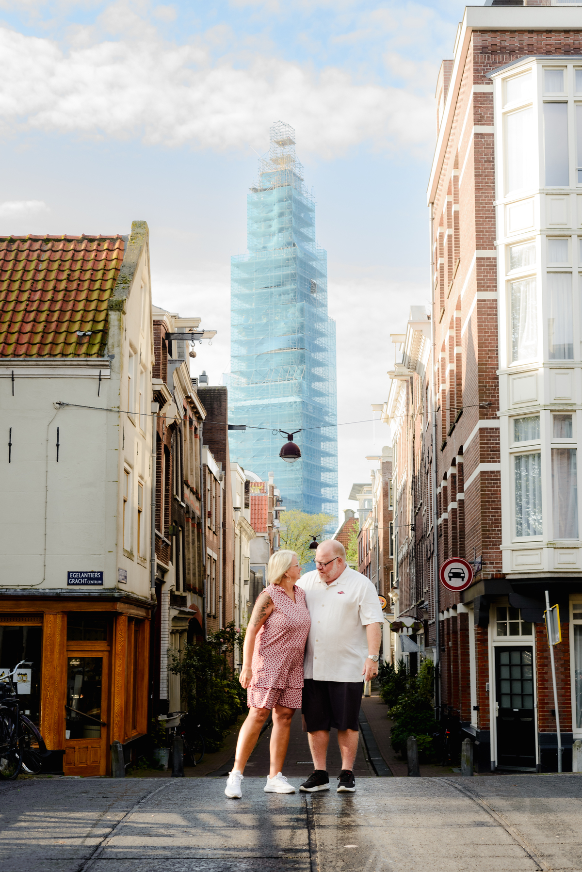 Couple holding hands and walking down a narrow street in Amsterdam, with a mix of old and new architecture surrounding them.