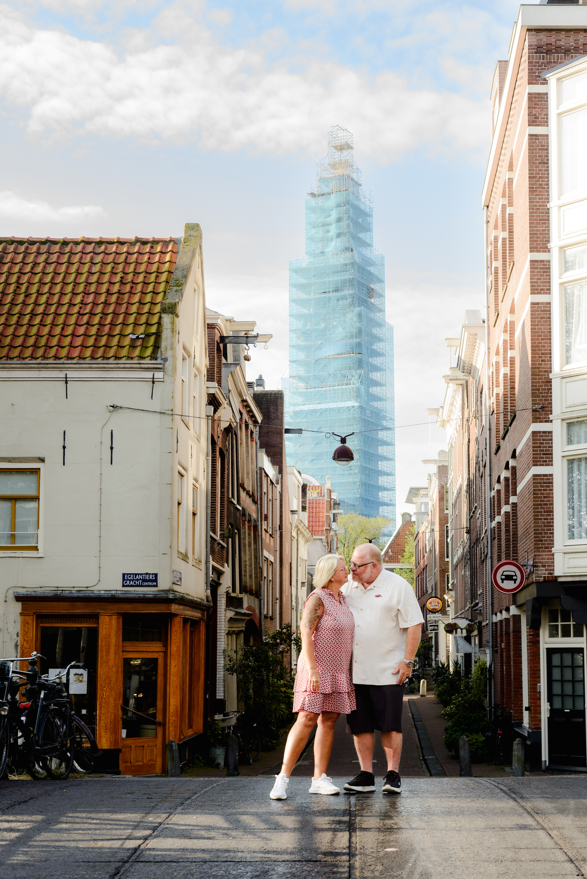 Couple posing together in front of a picturesque Amsterdam street, with the iconic Dutch houses and a tall modern building behind them.