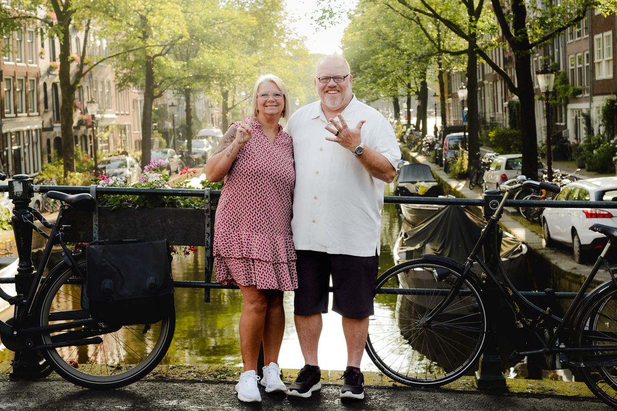 Couple celebrating with arms raised on an Amsterdam bridge, showcasing their joy and the beautiful cityscape around them.