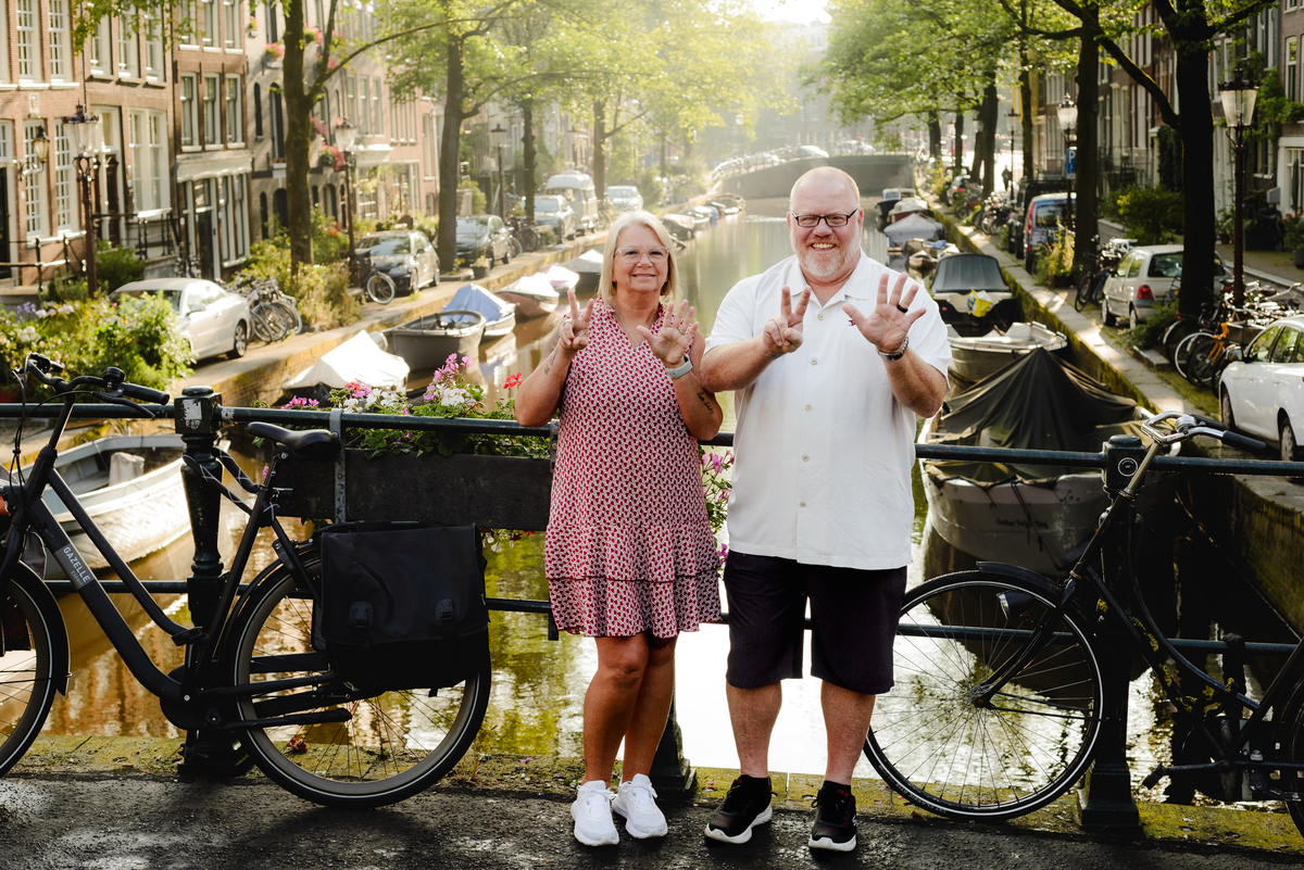 Couple celebrating with arms raised on an Amsterdam bridge, showcasing their joy and the beautiful cityscape around them.