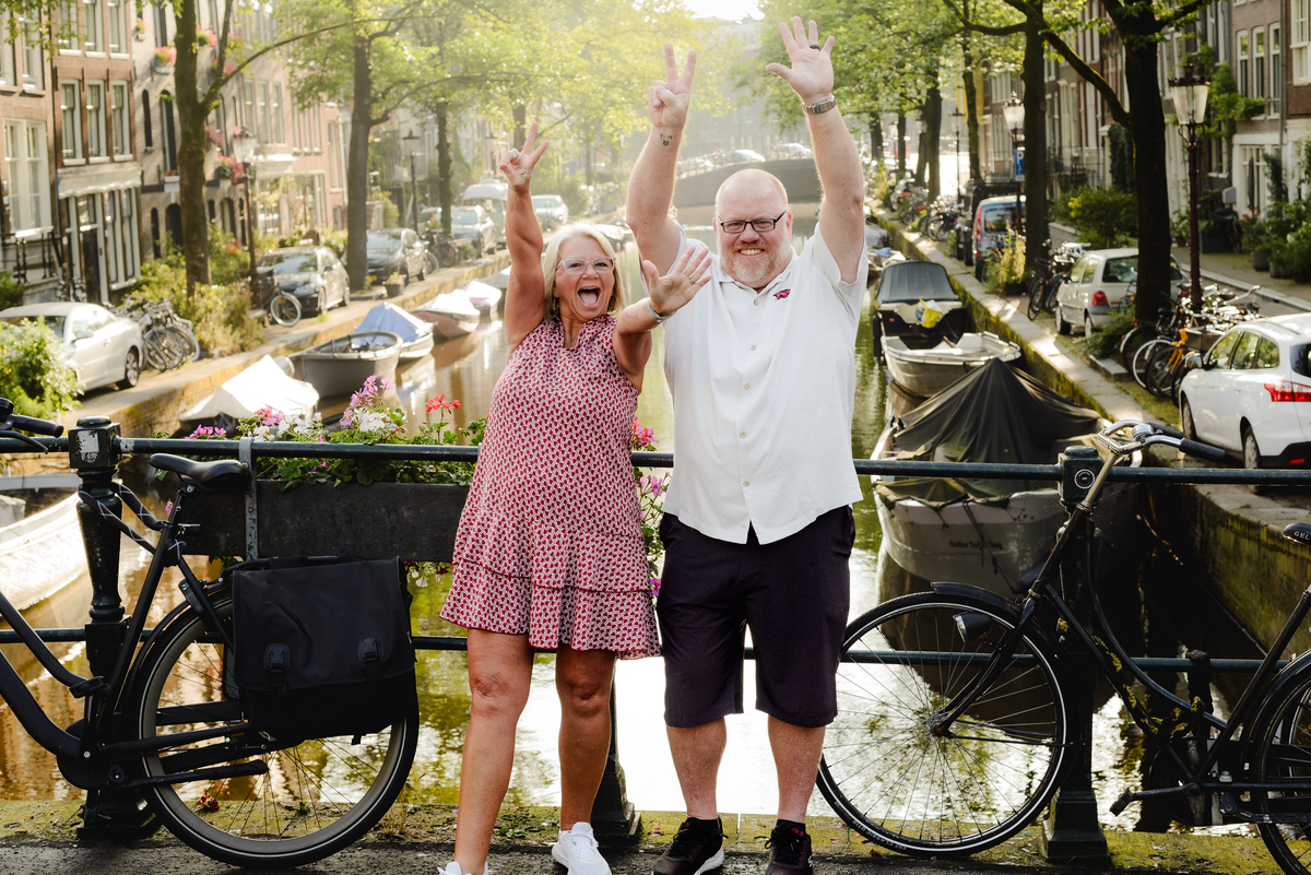 Couple celebrating with arms raised on an Amsterdam bridge, showcasing their joy and the beautiful cityscape around them.