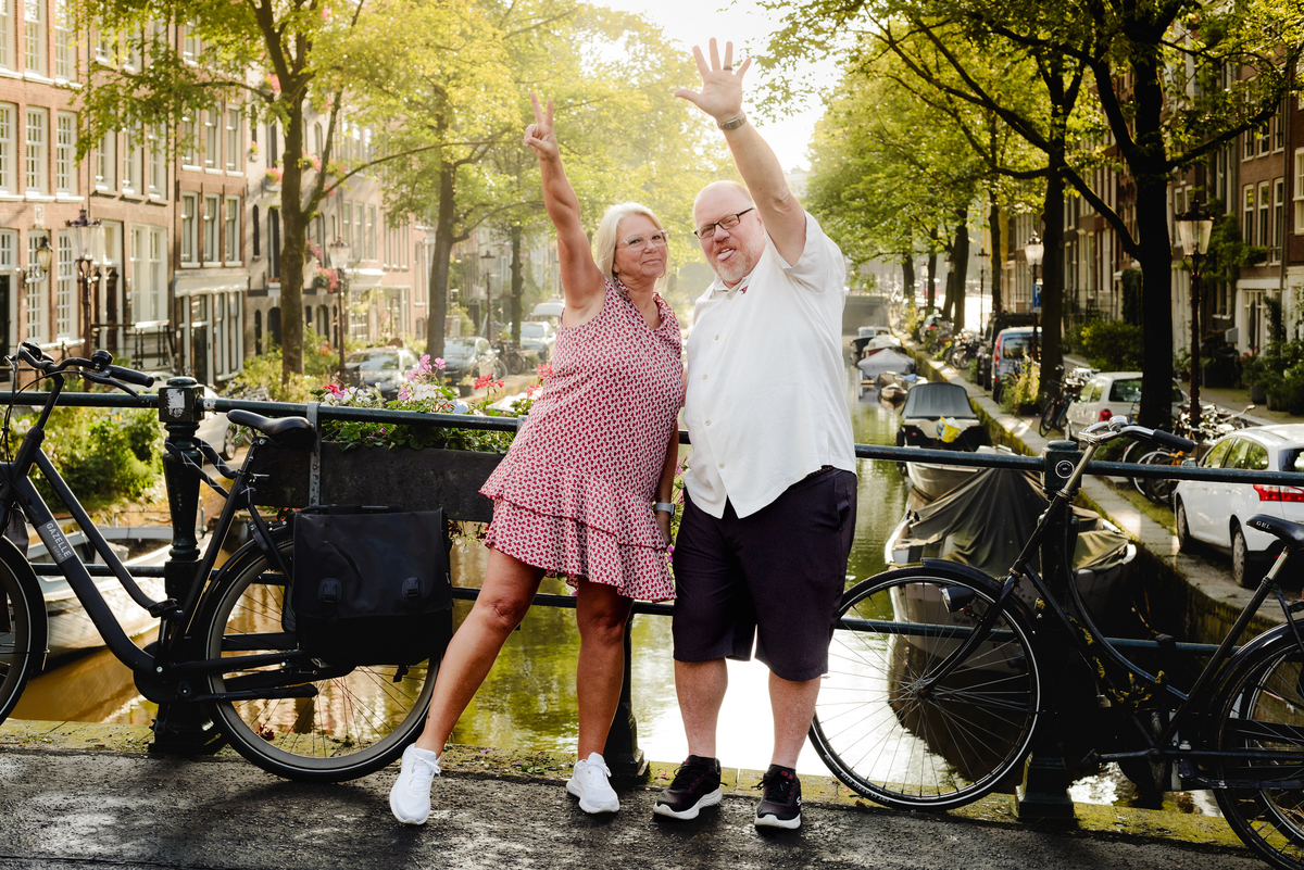 Couple celebrating with arms raised on an Amsterdam bridge, showcasing their joy and the beautiful cityscape around them.
