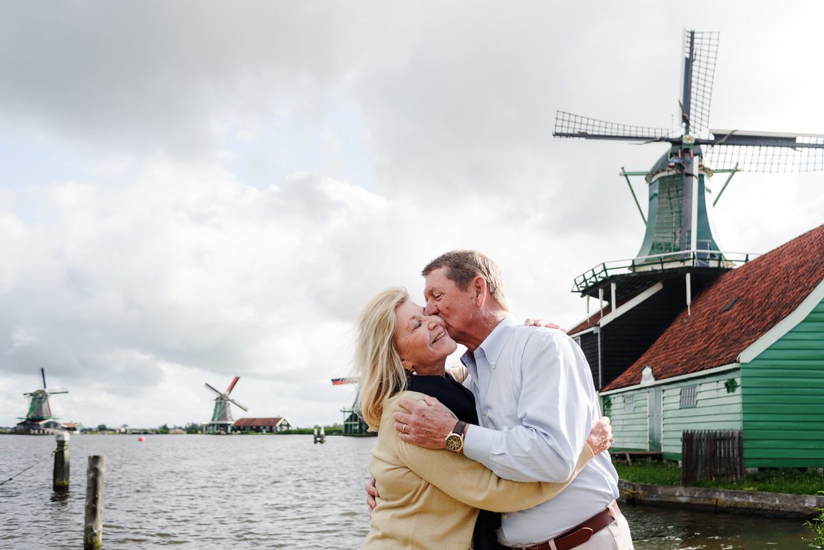 Couple sharing a kiss with picturesque windmills and a serene river view
