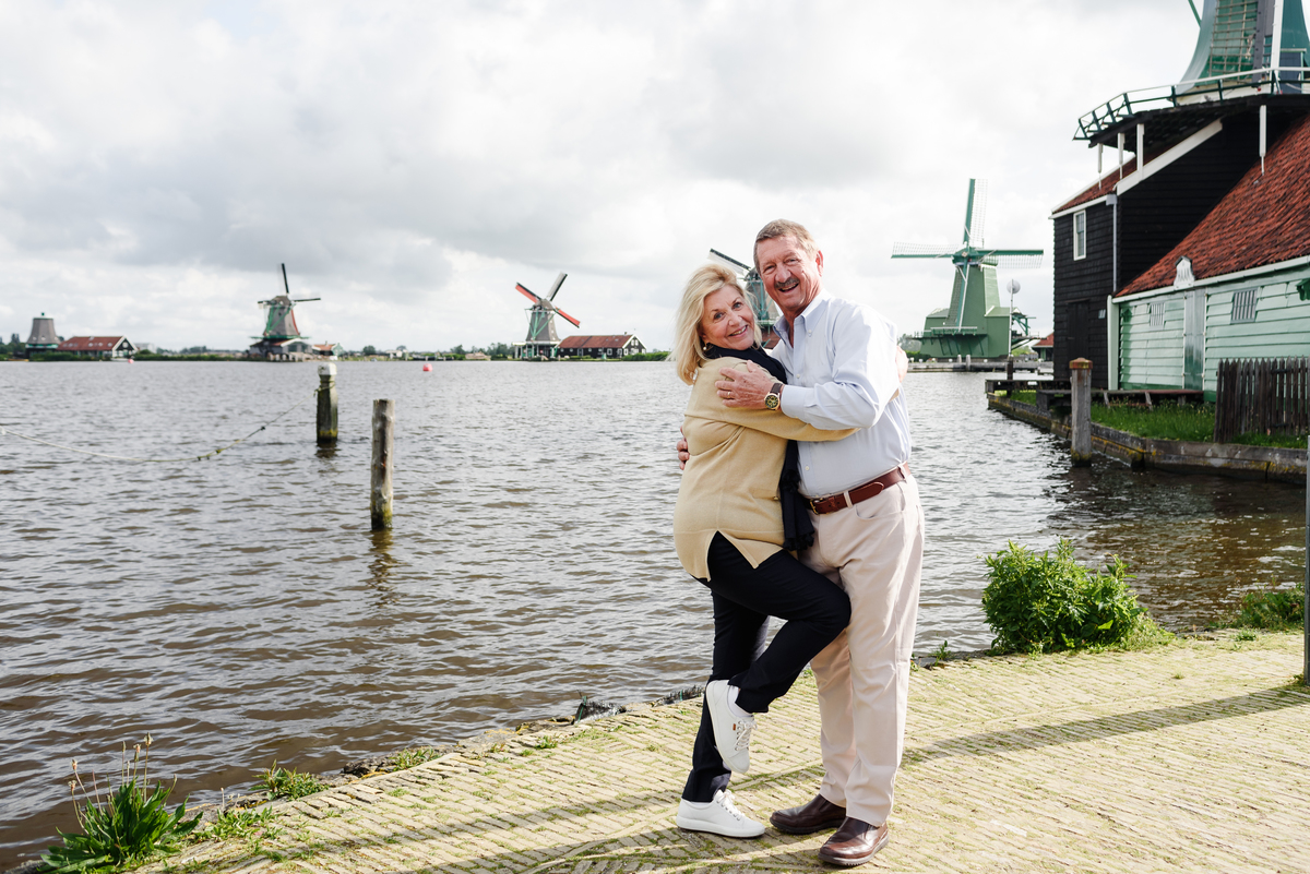 Couple embracing by the water, with traditional Zaanse Schans windmills behind them
