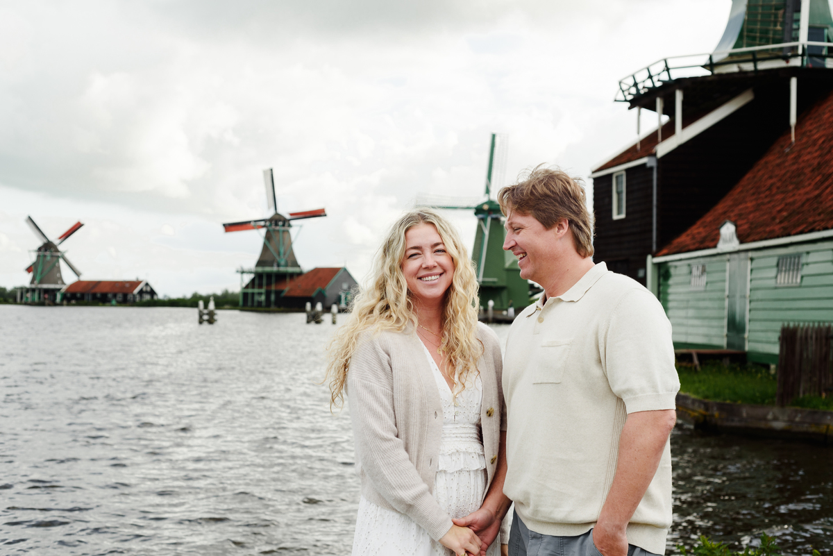 Couple holding each other close with windmills and a beautiful sky in the background.