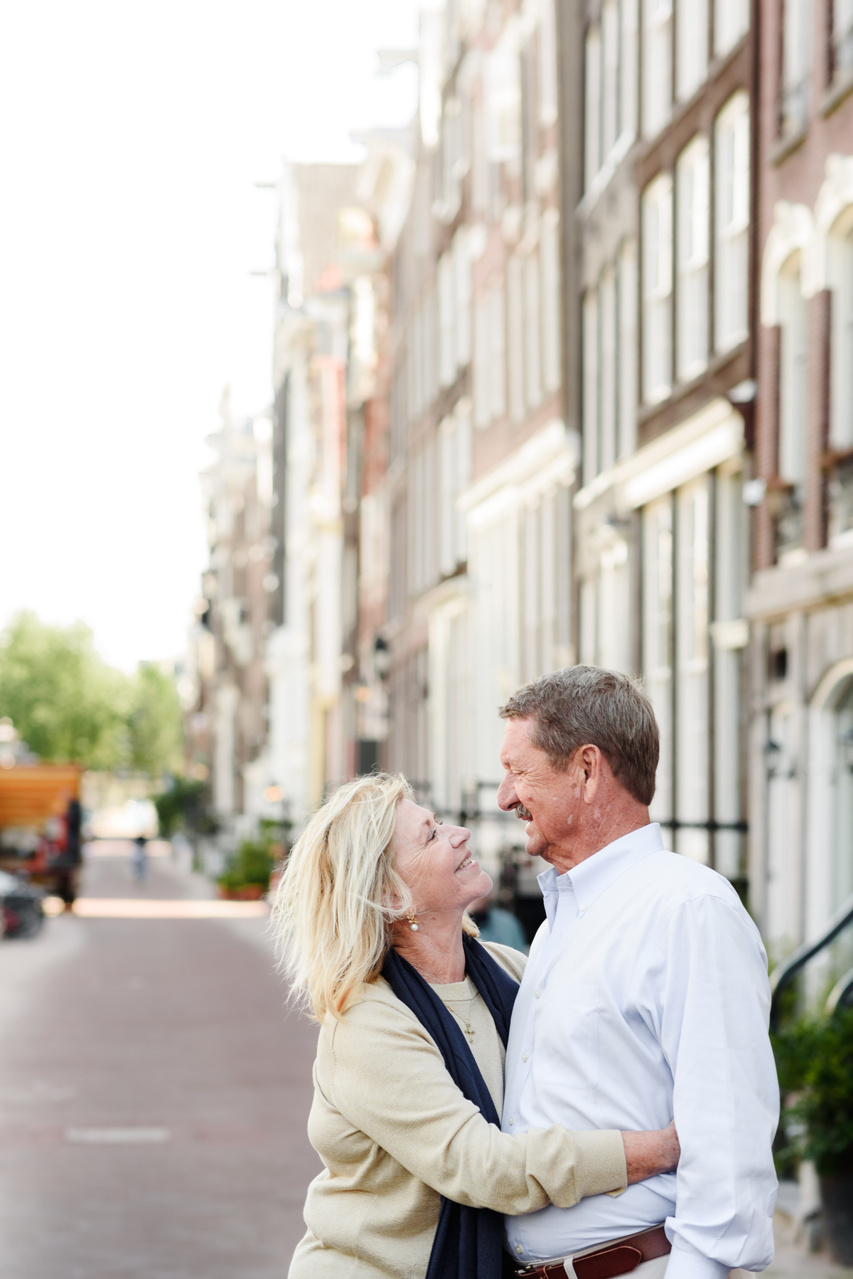 Couple holding hands and smiling at each other while walking through a charming Amsterdam street.