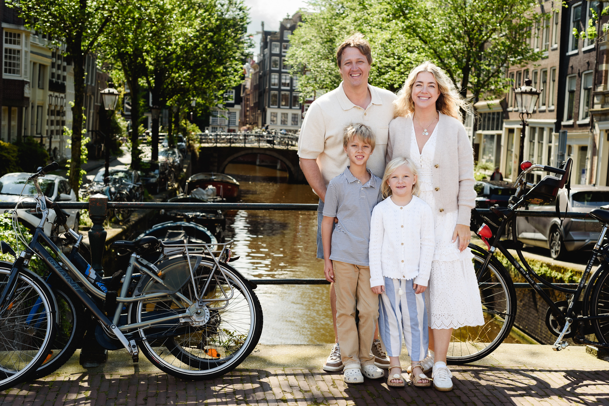 Family on a photo session in Amsterdam beside bicycles, with a scenic Amsterdam canal view behind them.