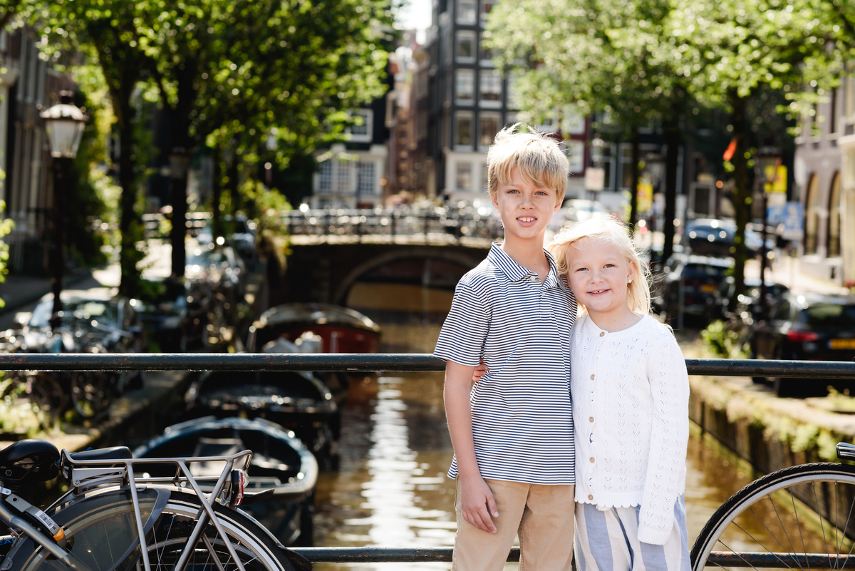 Family on a photo session in Amsterdam beside bicycles, with a scenic Amsterdam canal view behind them.
