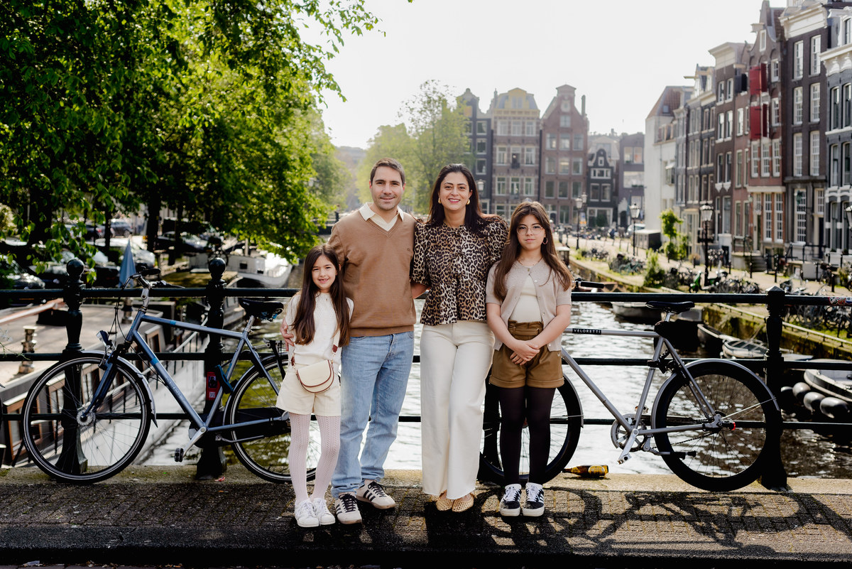 Family posing by the water, with beautiful Amsterdam townhouses in the background.
