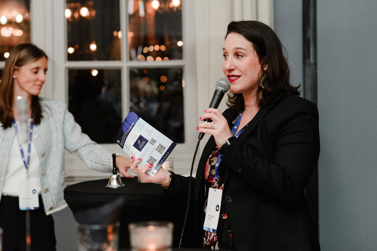 Event organizer speaking to a crowd of IE University alumni during the Networking Night, emphasizing the energy and structure of the event.