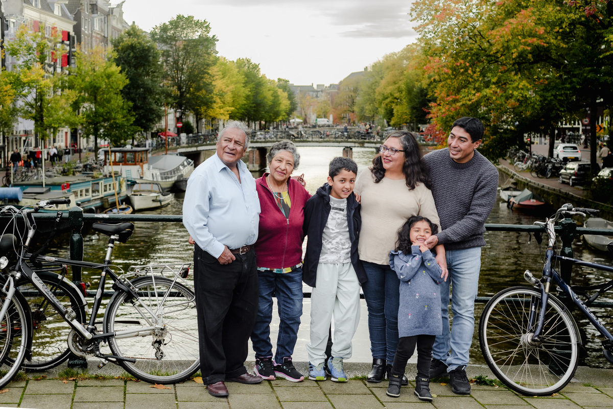 Multigenerational family from Peru posing together on a scenic Amsterdam bridge, featuring parents, two children, and grandparents smiling during their vacation photo session.