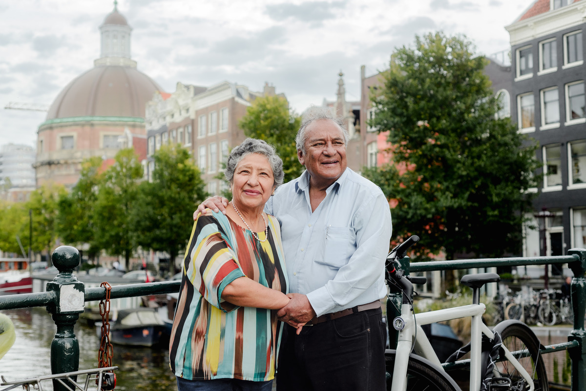 Grandparents sharing a laugh while standing on a cobblestone path in Amsterdam, with iconic canal houses in the background