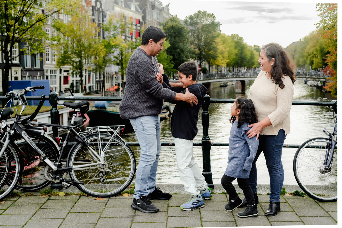 Parents playing with their two young children by the canal in Amsterdam, capturing a joyful and natural family moment during the photo session.