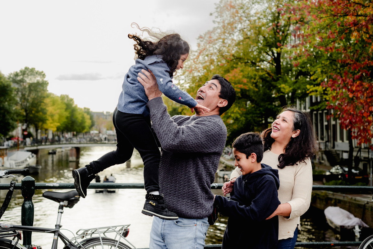 Parents playing with their two young children by the canal in Amsterdam, capturing a joyful and natural family moment during the photo session.
