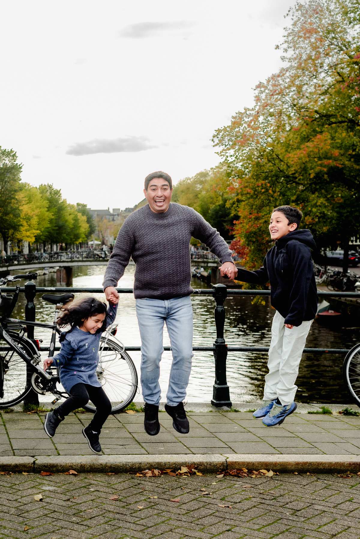 Parents playing with their two young children by the canal in Amsterdam, capturing a joyful and natural family moment during the photo session.