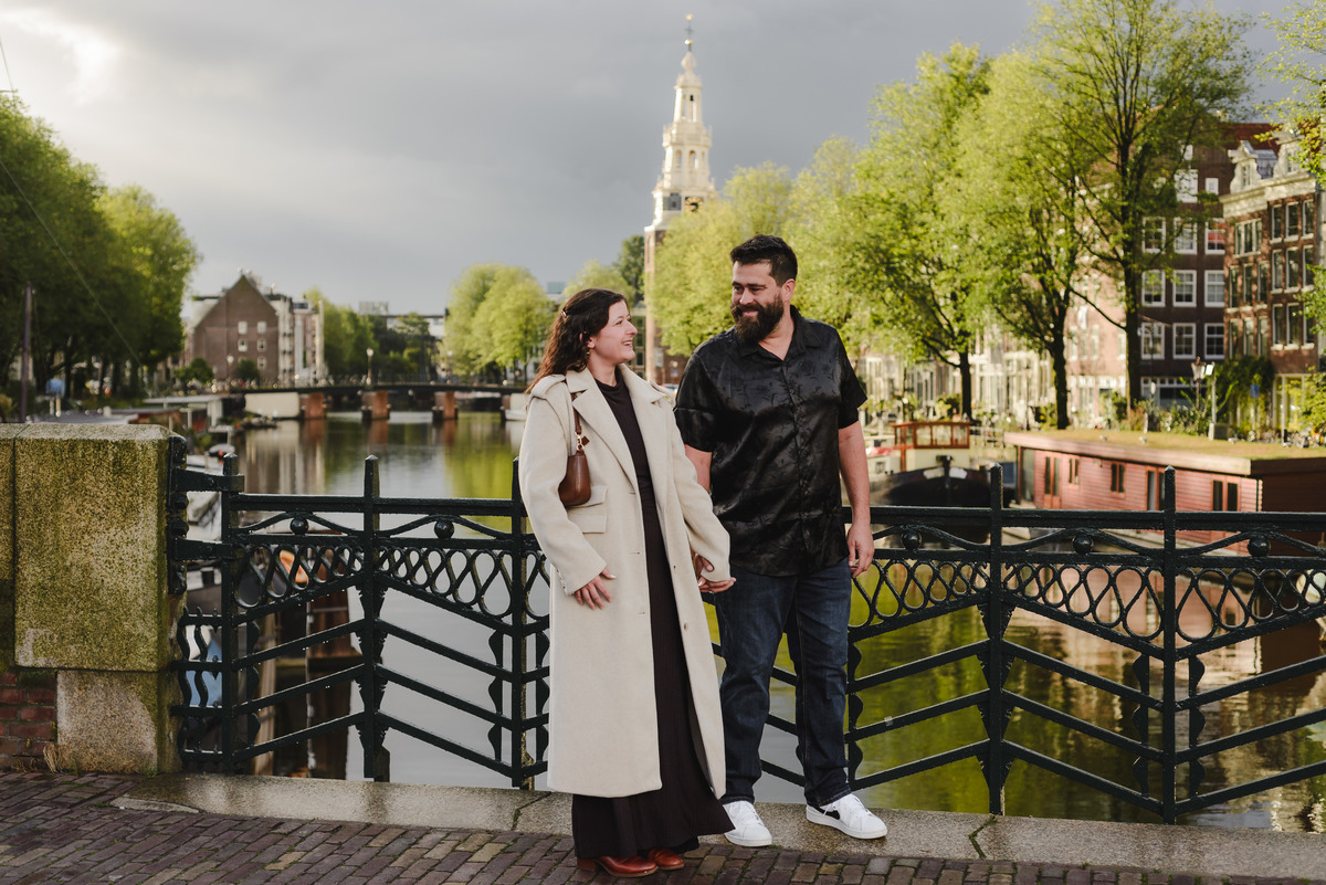ouple holding hands, strolling through the quiet streets near Oude Waal in Amsterdam, with a historic tower in the background