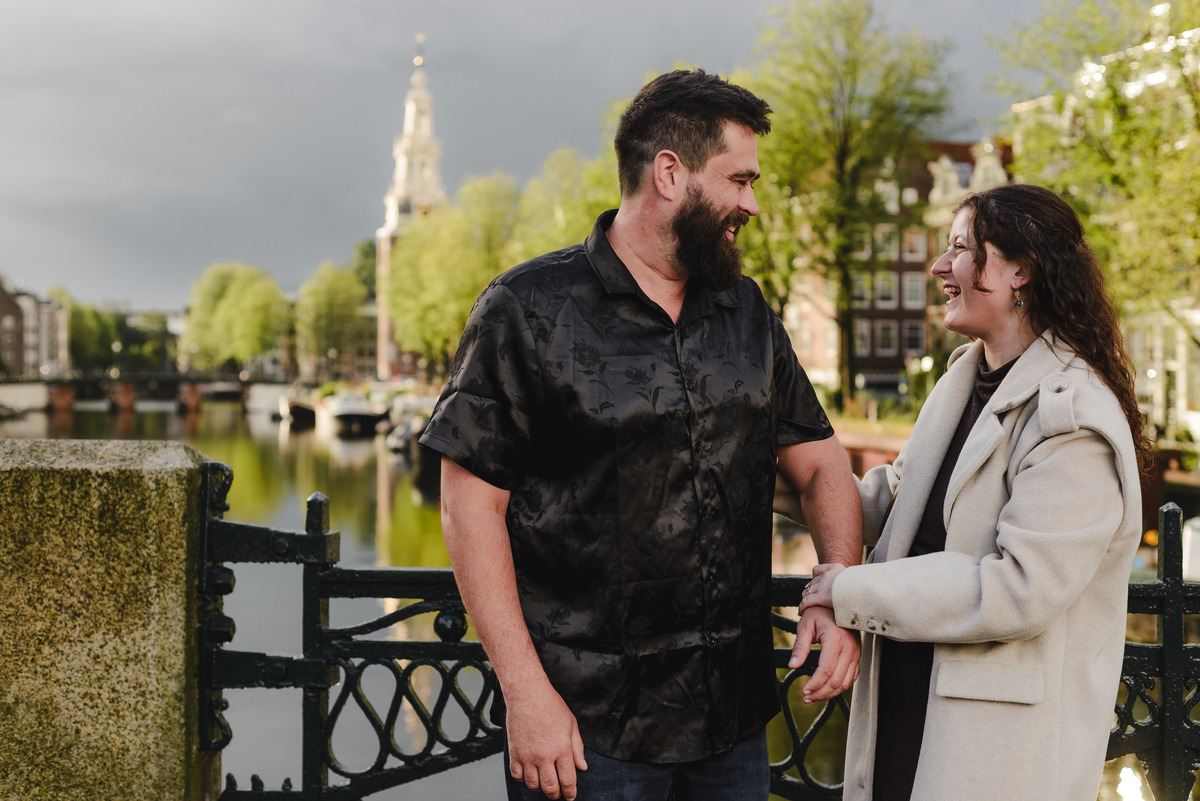 ouple holding hands, strolling through the quiet streets near Oude Waal in Amsterdam, with a historic tower in the background
