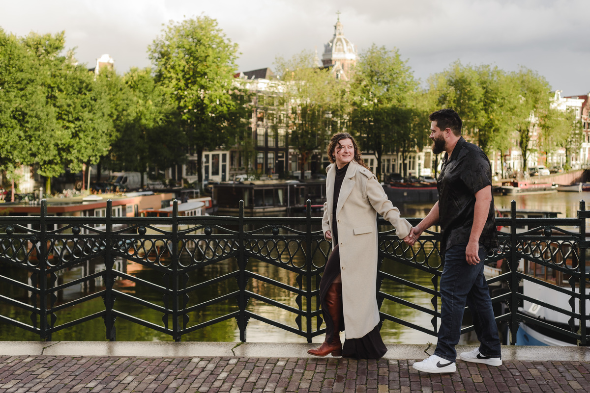 ouple holding hands, strolling through the quiet streets near Oude Waal in Amsterdam, with a historic tower in the background