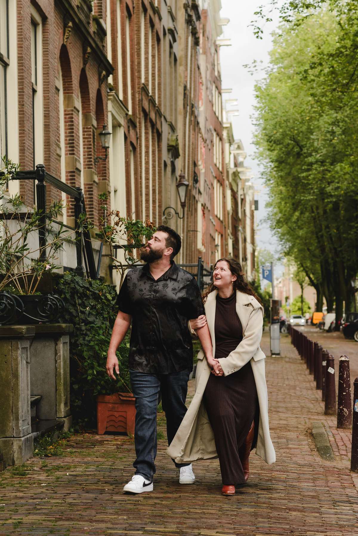 ouple holding hands, strolling through the quiet streets near Oude Waal in Amsterdam, with a historic tower in the background