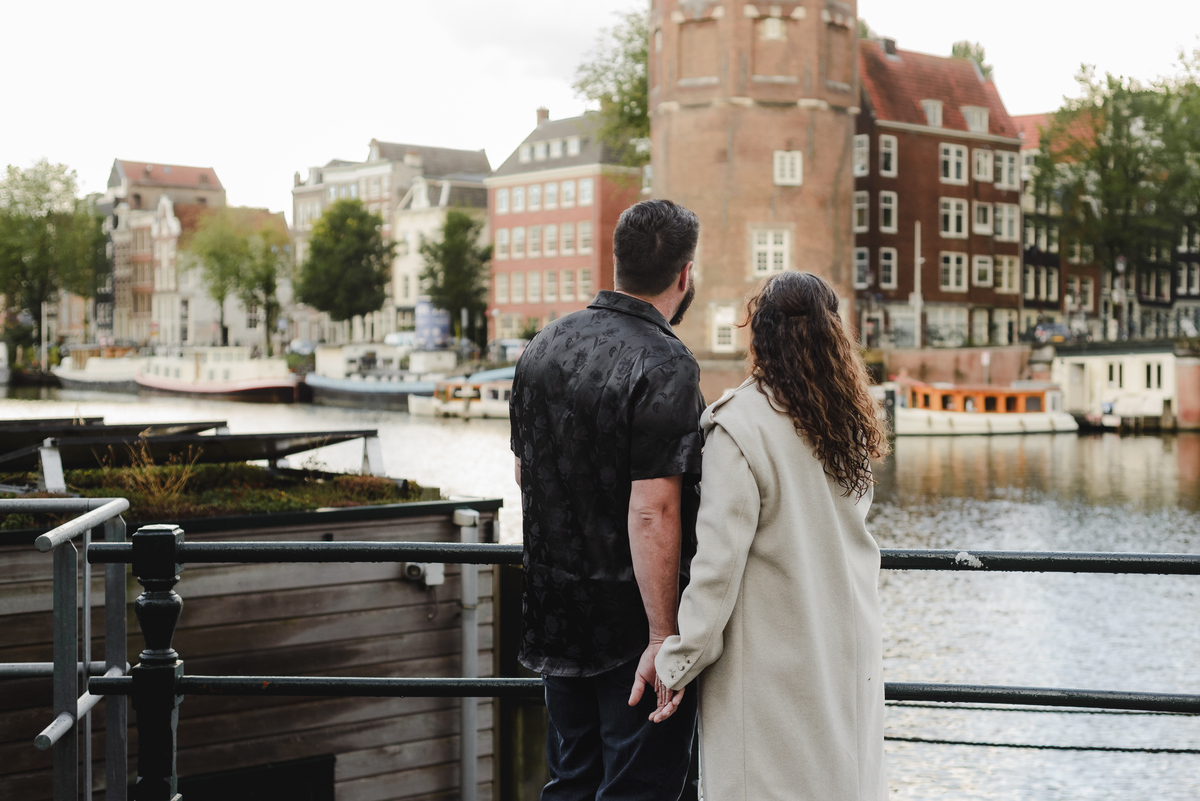 Engaged couple standing on a bridge at Oude Waal, overlooking a picturesque canal and historic tower on a moody, post-rain day in Amsterdam